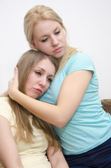 Pretty young girl comforting her friend, holding her in her arms