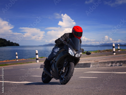 Fototapeta na wymiar young biker man riding motorcycle on asphalt road against beauti