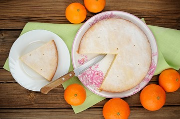 Cut clementine pie with clementines and knife on wooden backgrou