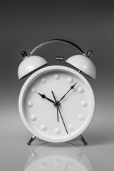 White metal alarm clock with two bells on grey gradient backgrou