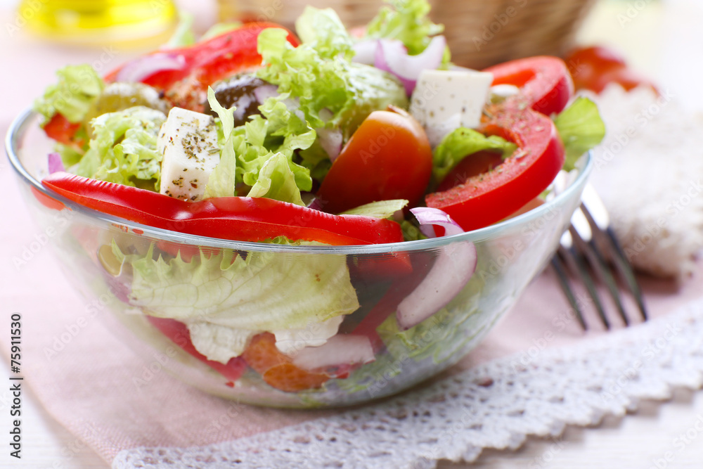 Greek salad in glass dish with fork and vegetables background