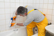 © sima - Worker plumber caulking bath tube and tiles with silicone glue