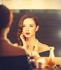 Poster - Portrait of a beautiful woman as applying makeup near a mirror