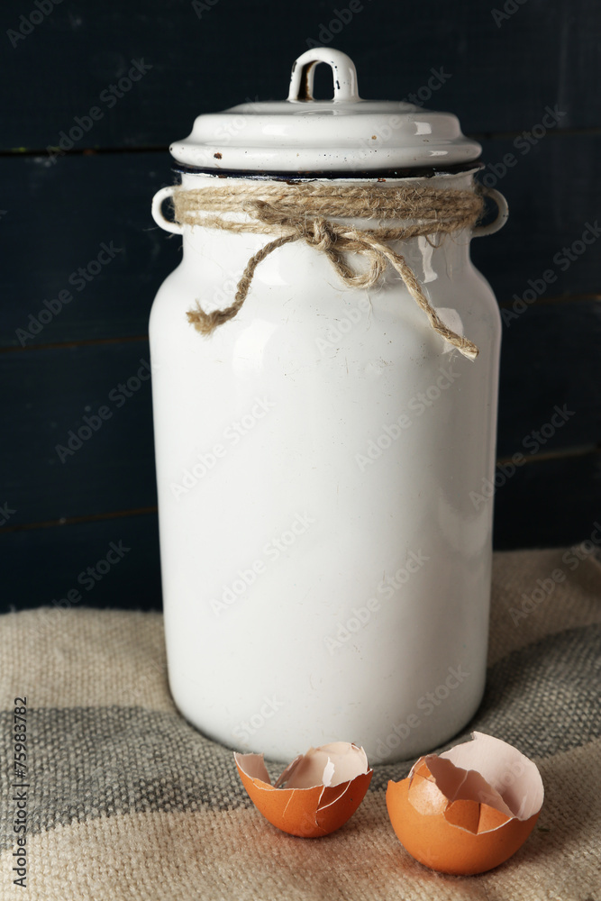 Milk can with eggshell on color wooden background