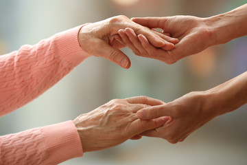 Wall Mural - Old and young holding hands on light background, closeup