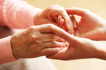 Wall Mural - Old and young holding hands on light background