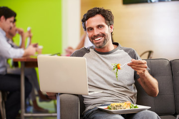 Wall Mural - Man Sitting On Sofa And Eating Lunch In Design Studio