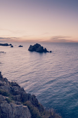 Little stone island in the ocean seen from the cliffs at sunset