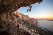 Rock climber climbing on roof in cave, his partner belaying
