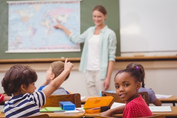 Cute pupil smiling at camera at his desk in classroom