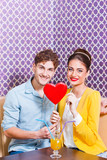 Fototapeta Panele - Cute young couple sitting at the table holding a heart