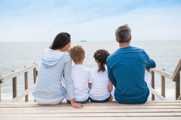 family back sitting on a wood pontoon at seaside watching the ho