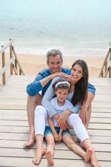 happy family sitting on a wooden pontoon in front of the sea