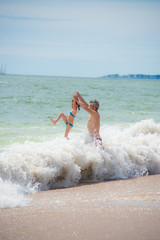 A young girl is playing with her dad in the sea waves