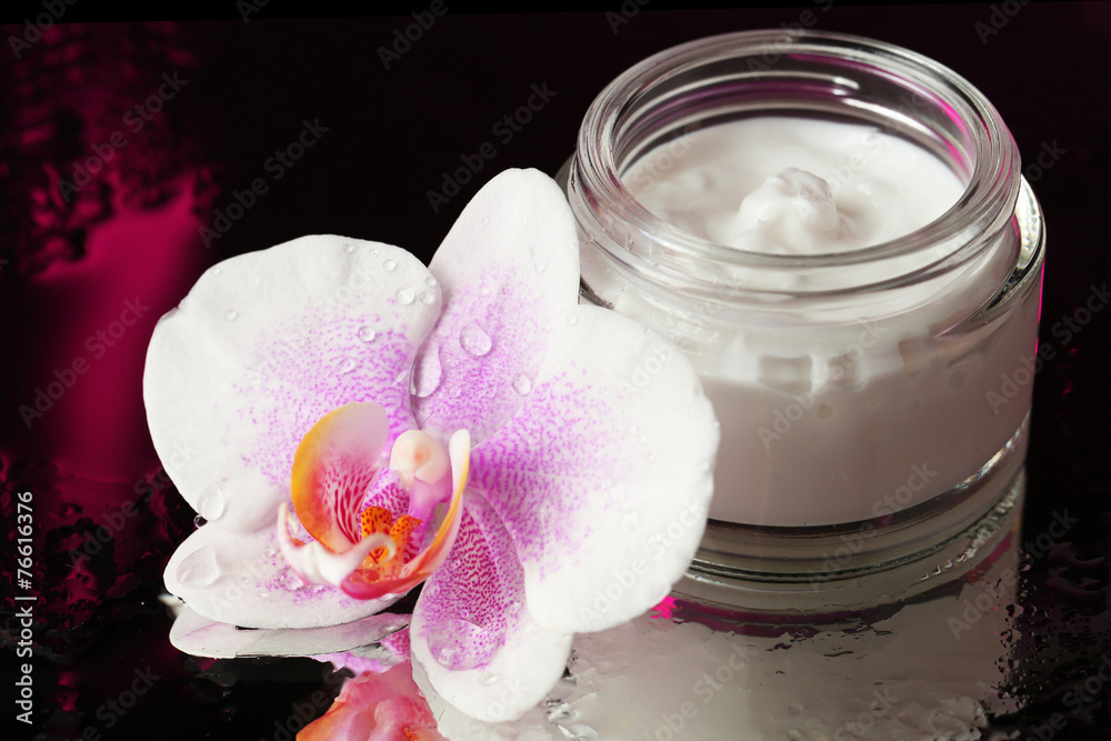 Face cream with orchid flower on dark background