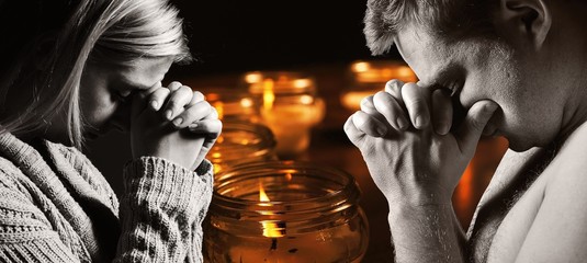 Praying man and woman with candles on background.