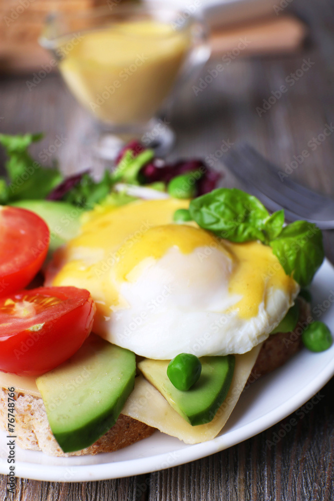 Toast with egg Benedict and avocado on plate on wooden table
