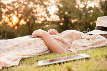Young Woman Taking A Nap In Park With Hat Over Face With Tablet