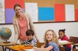 © WavebreakMediaMicro - Pretty teacher helping pupil in classroom smiling at camera