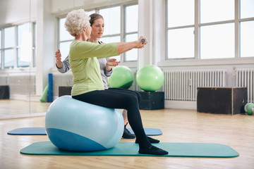 Female trainer assisting senior woman lifting weights