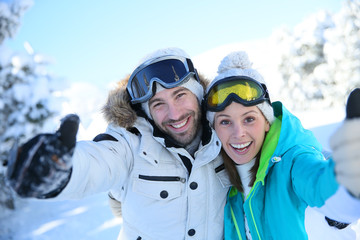 Wall Mural - Cheerful couple of skiers showing thumbs up