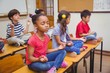 © WavebreakMediaMicro - Mixed race pupils meditating in lotus position on desk in classroom