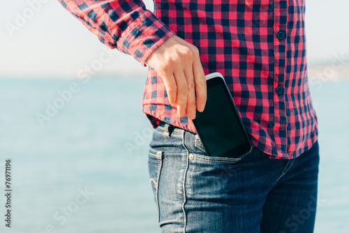 Fotografía Woman takes out phone of her pocket on beach