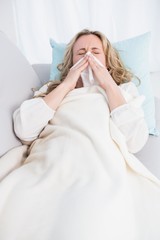 Wall Mural - Blonde lying on couch sneezing on tissue