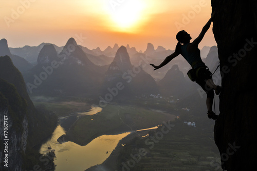 Naklejka ścienna Female climber silhouette against the sunset over the river