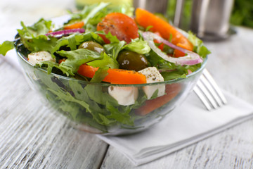 Wall Mural - Greek salad in glass dish on napkin and color wooden background