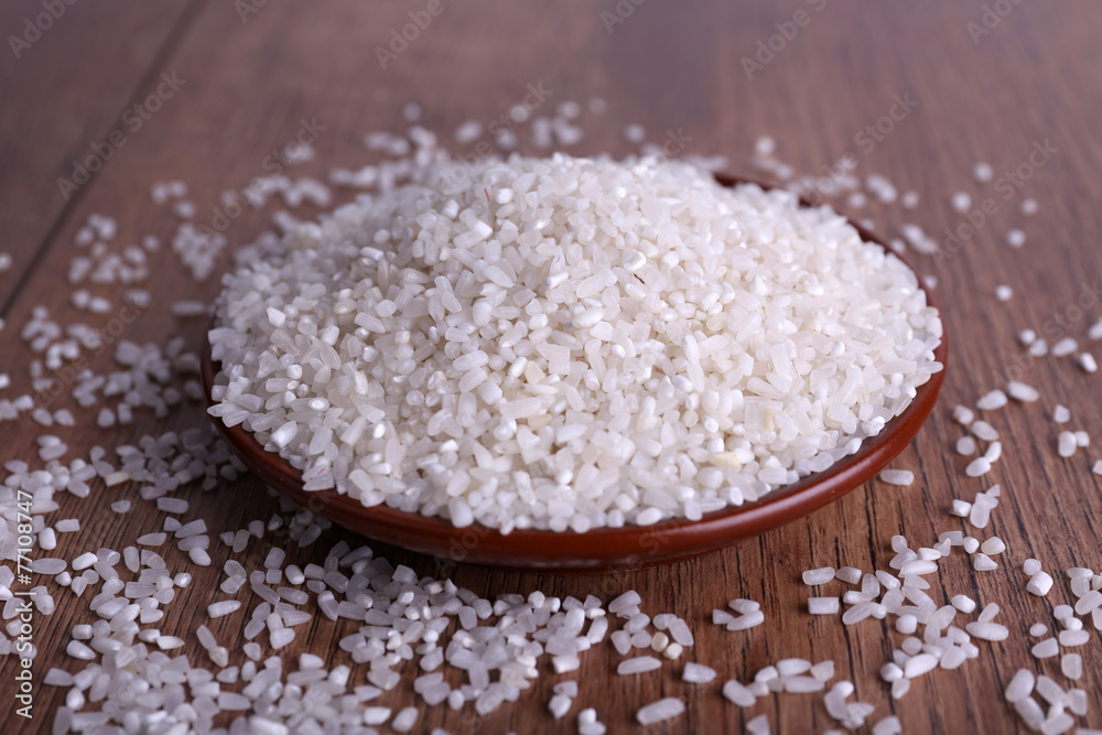 Grain of rice on plate on wooden background