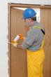 © sima - Worker installing wooden door, using polyurethane foam