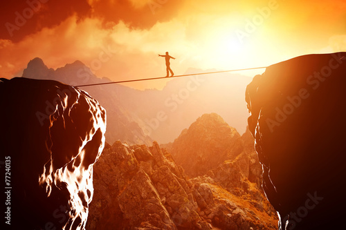 Cuadros en Lienzo Man walking and balancing on rope over precipice in mountains