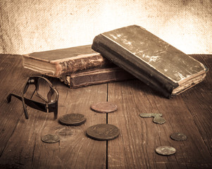 Vintage books and coins and spectacles on old wooden table. Tone