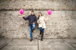 © bokan - Young couple leaning on the wall holding pink balloons.