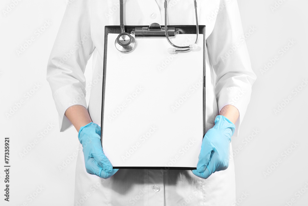 Doctor holding clipboard on light background