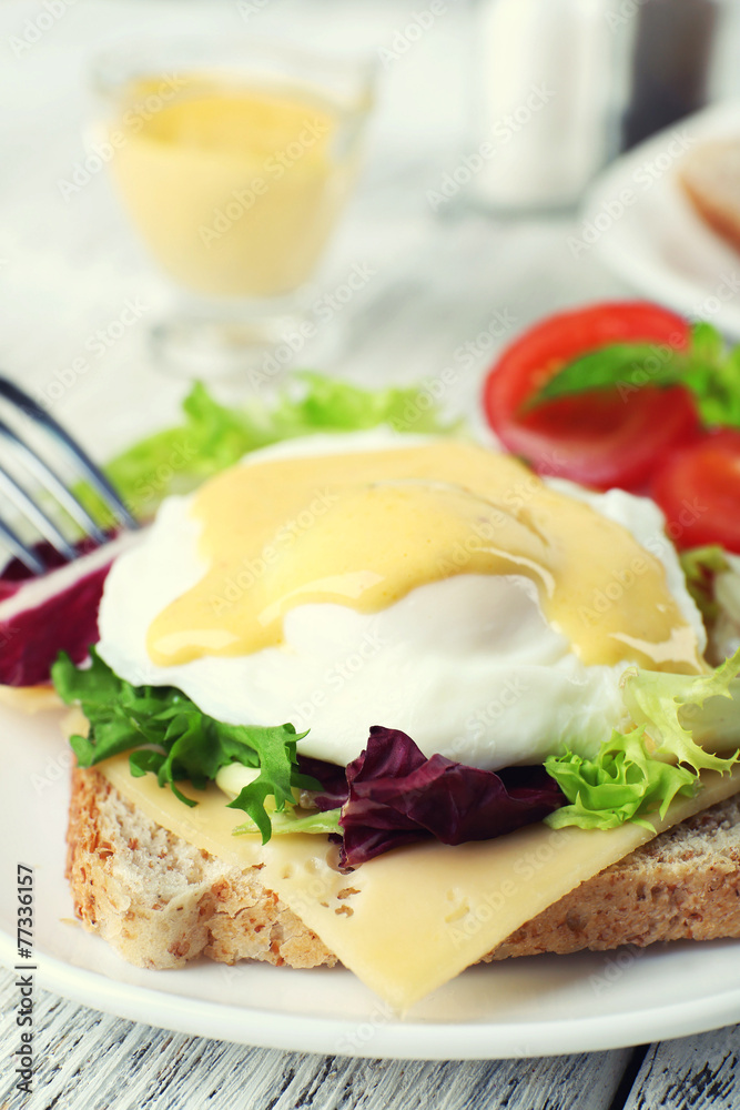 Toast with egg Benedict and tomato on plate on wooden table