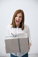 Poster - Portrait of a surprised woman holding gift over gray background