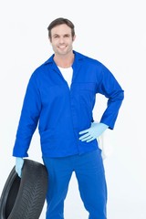 Poster - Mechanic holding tire while standing with hand on hip