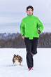 junger Mann joggt mit Hund in verschneiter Winterlandschaft