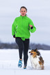 junge Frau joggt mit Hund (Shetland Sheepdog) im Schnee