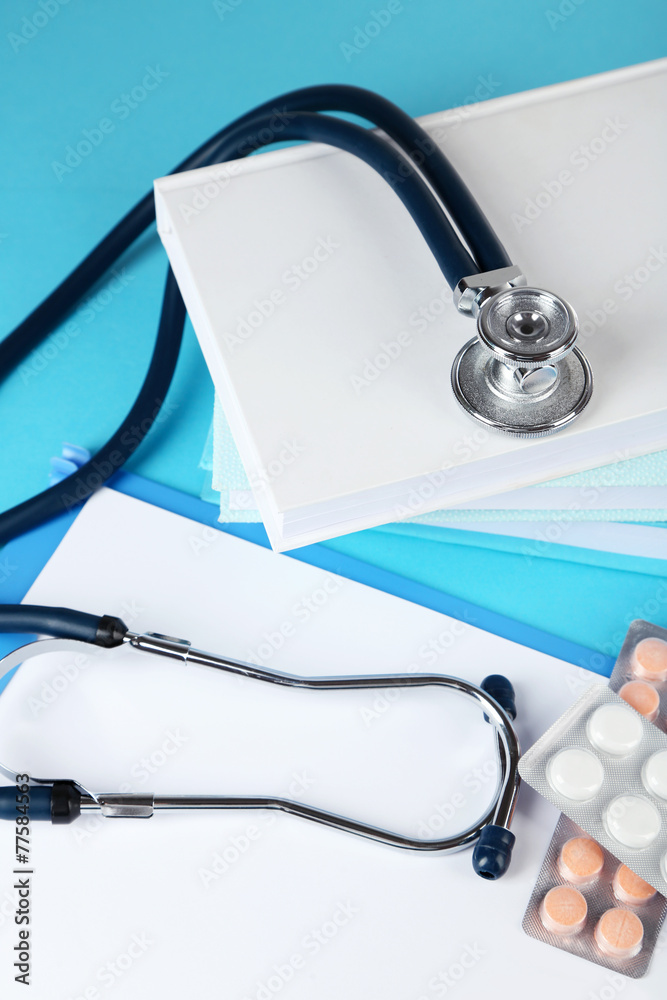Medical stethoscope with books and tablet on blue background