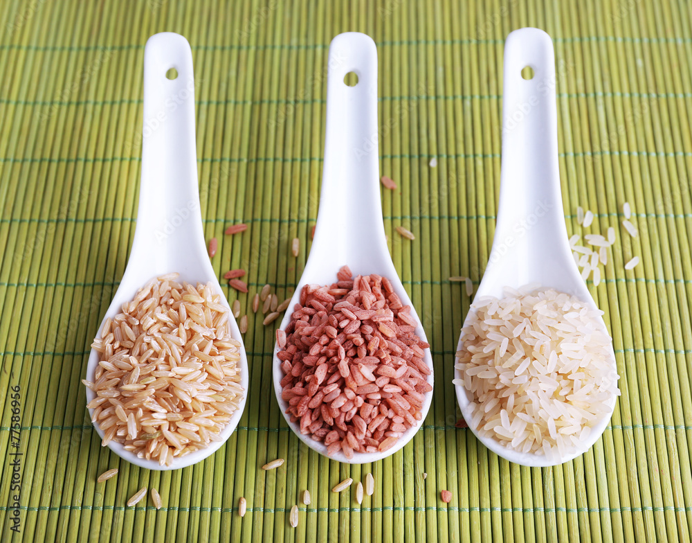 Different types of rice in spoons on bamboo background