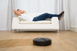 © Andrey Popov - Robotic Vacuum Cleaner In Front Of Man Relaxing