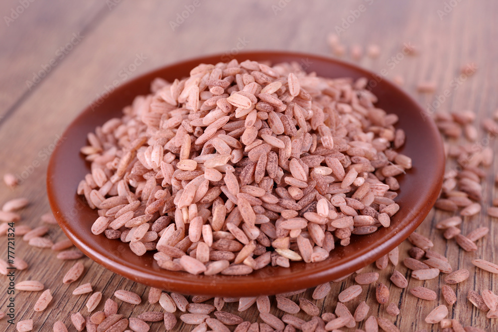 Red rice on plate on wooden background