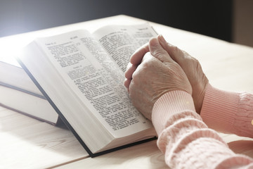 Hands of old woman with Bible on table, close-up