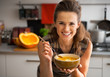 © Alliance - Happy young woman eating pumpkin soup in kitchen