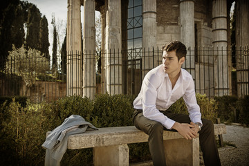 Wall Mural - Handsome young man in European city, sitting on stone bench