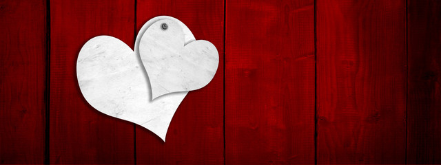 Conceptual two white old paper vintage hearts on red wood