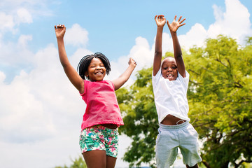 Two African kids jumping in park.